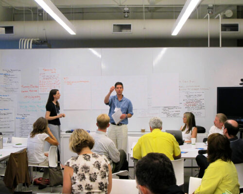 Nadav Malin in front of large whiteboard facilitating classroom style discussion