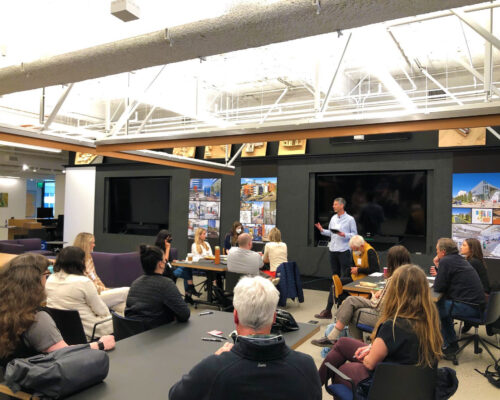Nadav Malin in front of black screen facilitating group seated at tables