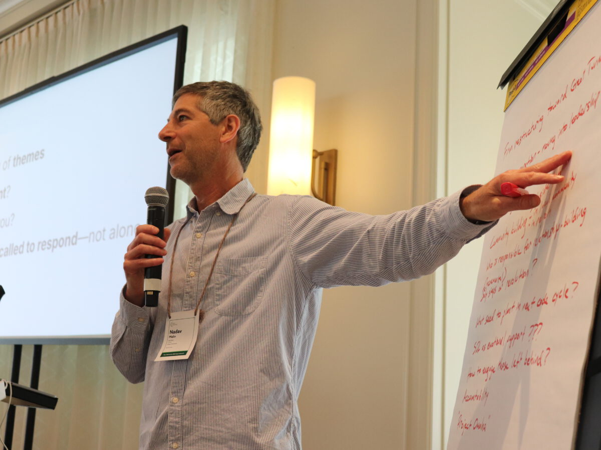 Nadav Malin with mic pointing to summary session content